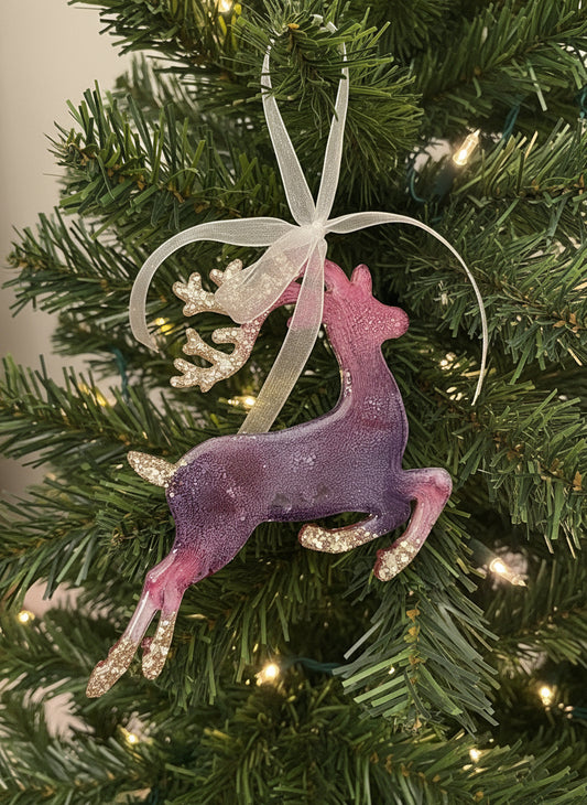 Purple glittery reindeer ornament held in a hand with a Christmas tree in the background